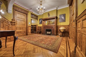 A room with a large wooden door, a fireplace, a globe, and a chandelier.
