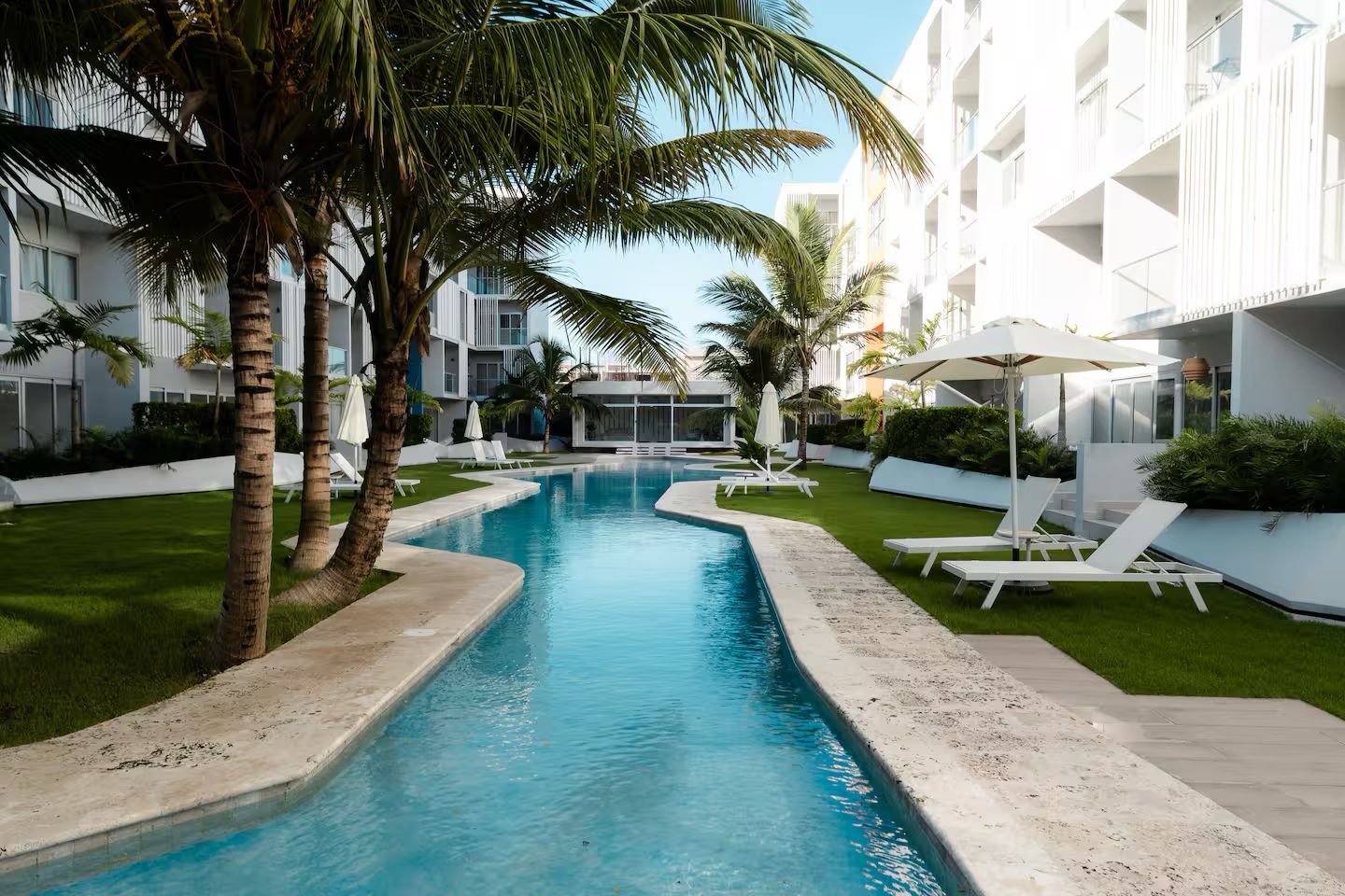 Piscina com espreguiçadeiras e palmeiras, cercada por um edifício moderno.