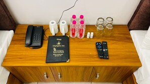 A wooden table with a black telephone, two white water bottles, a black menu book, a pair of glasses, and a remote control.