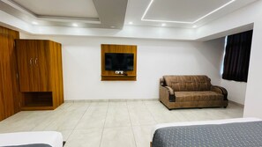A modern bedroom with a bed, a wooden wardrobe, a sofa, and a TV mounted on the wall. - Citylights Inn Hotel (Prayagraj)