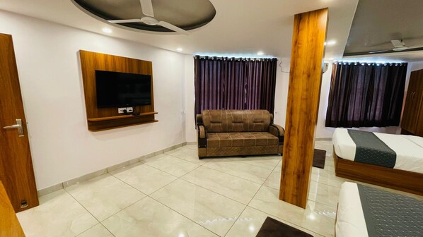 Una habitación de hotel con televisor de pantalla plana montado en la pared, un sofá, una cama con cabecera de madera y un ventilador de techo.