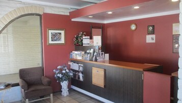 Un mostrador de recepción con encimera de madera, una silla, un florero con flores y un reloj de pared.