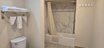 Un baño con inodoro, toallero con toallas dobladas, ducha con pared de mármol y bañera.