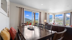 A dining area with a table, chairs, and a view of mountains through large windows. - New 3BR Condo Within Walking Distance to Marina and Mins From Ski Resorts! (Dillon)