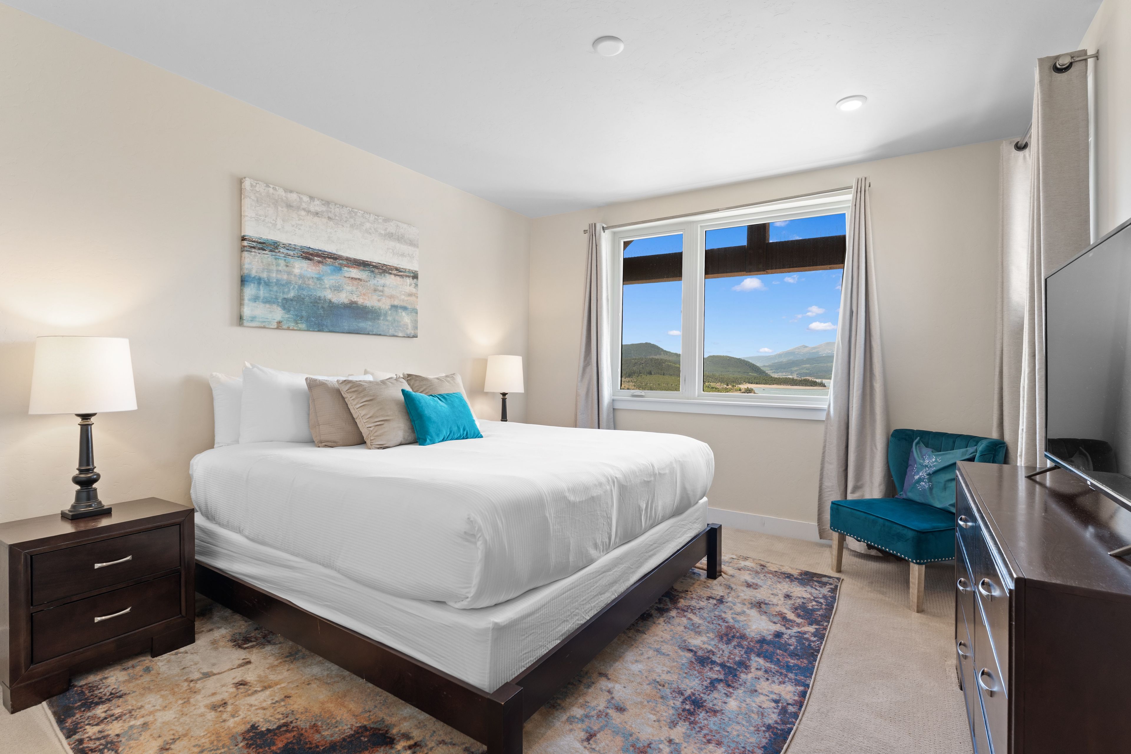A bedroom with a large bed, bedside lamps, a desk, a TV, and a window with a view of the outdoors.