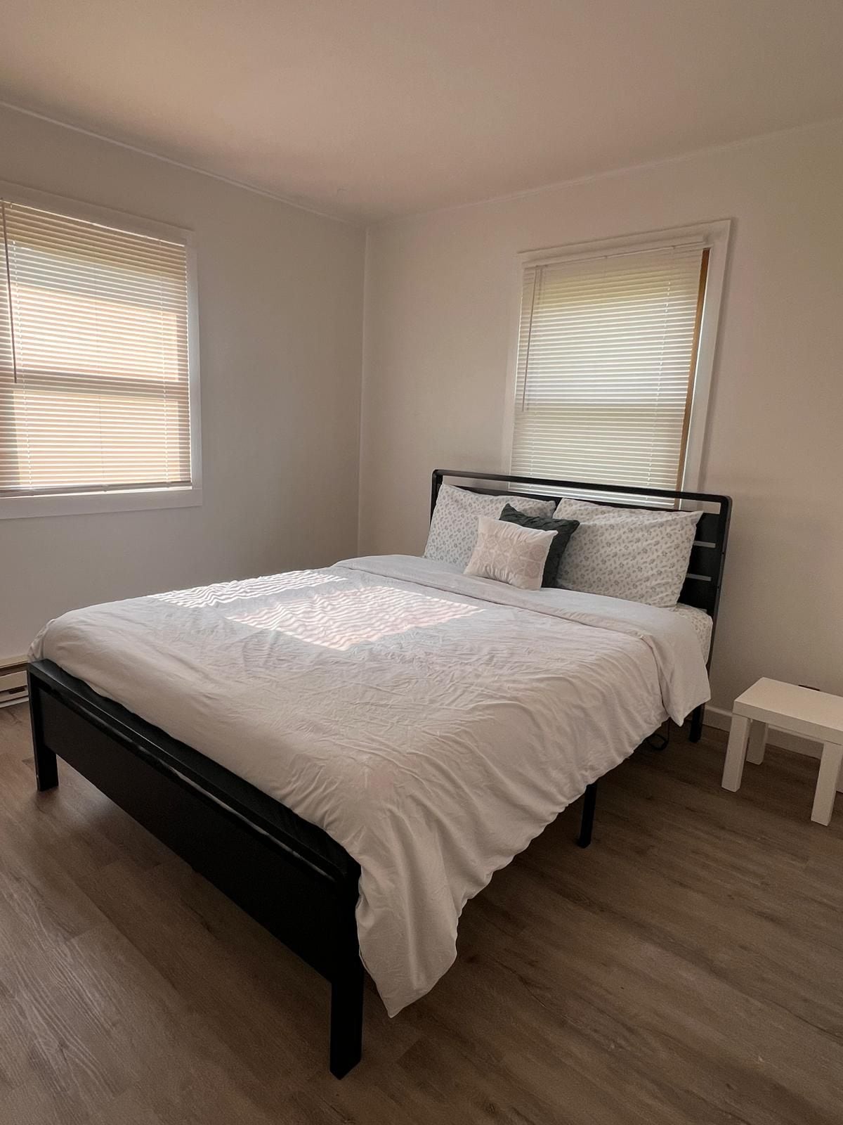 A bedroom with a bed, two windows, and a small bedside table.