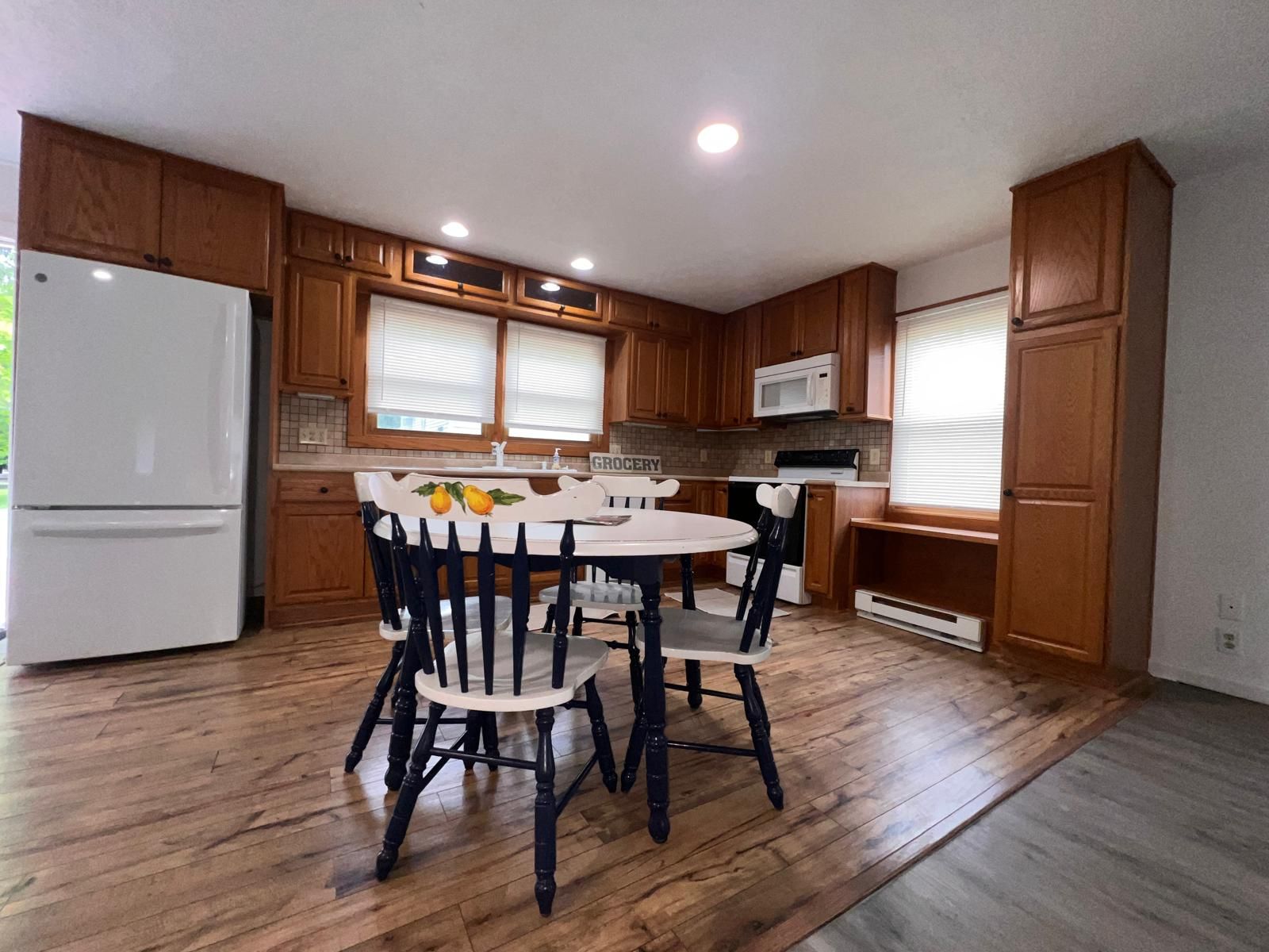 A kitchen with wooden cabinets, a white refrigerator, a microwave, and a dining table with chairs.