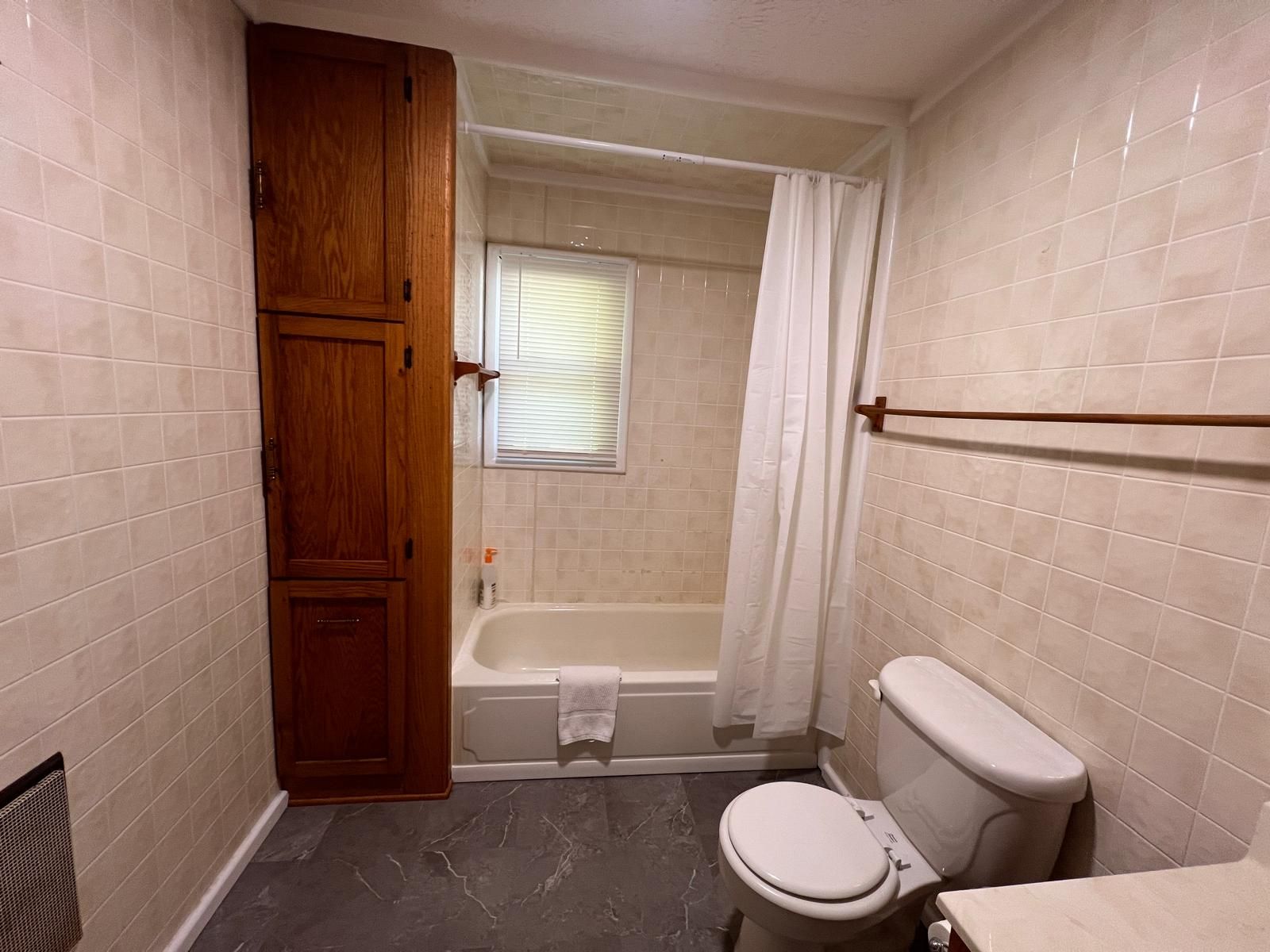 A bathroom with a bathtub, toilet, and wooden cabinet.