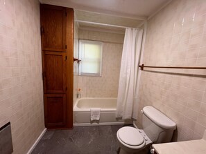 Een badkamer met een badkuip, toilet en een houten kastje.