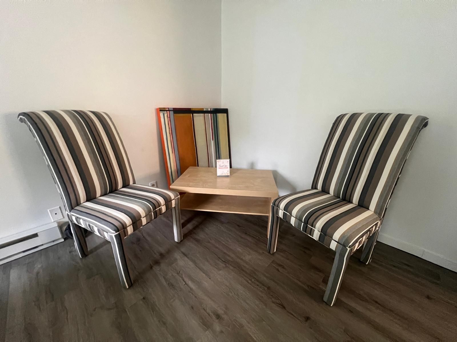 Quarto de canto com duas poltronas listradas e uma pequena mesa de madeira.