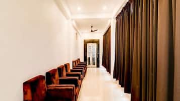 A hotel corridor with rows of wooden chairs, a ceiling fan, and a door at the end.