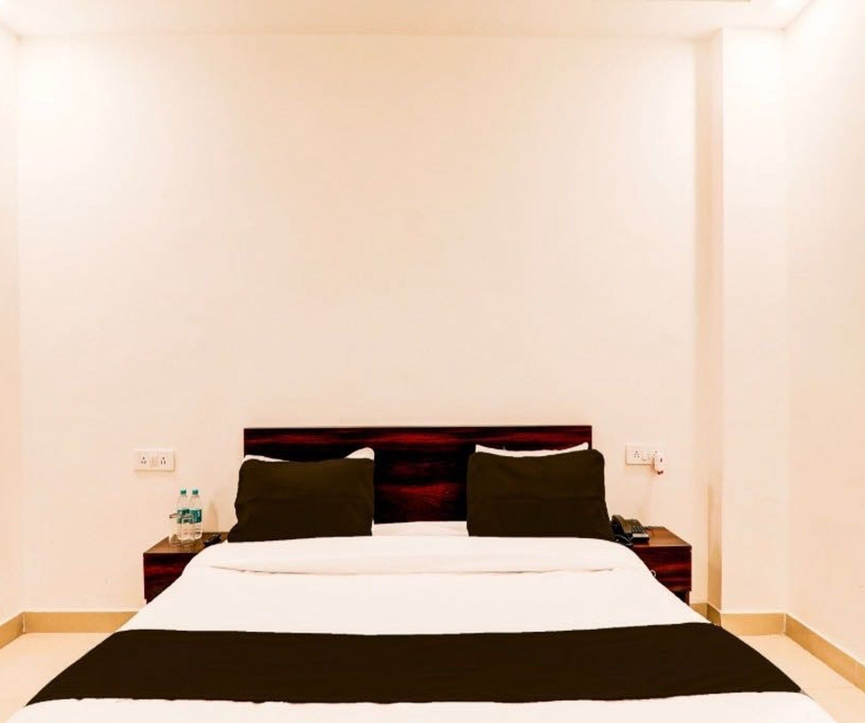 A hotel room with a large bed, a nightstand with a phone, and a wall socket.