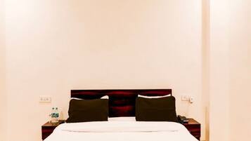 A hotel room with a large bed, a nightstand with a phone, and a wall socket.