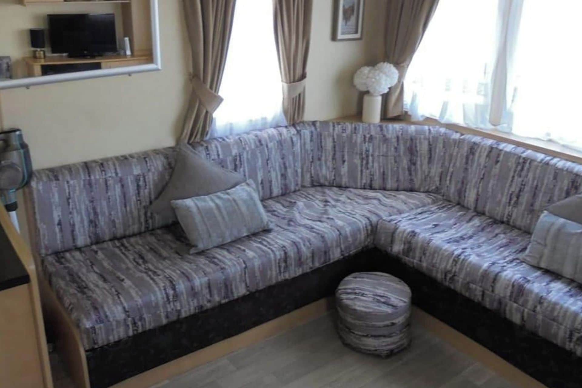 A corner sofa with a patterned fabric, a round ottoman, and a television on a stand.