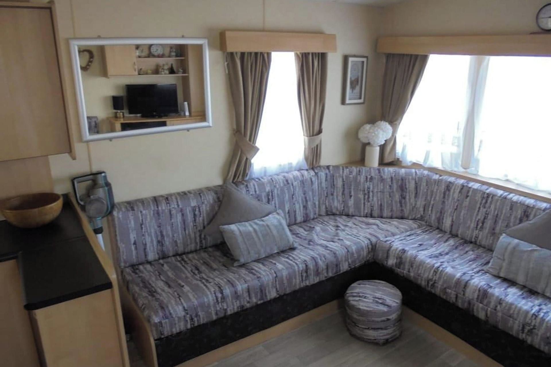 Een gezellige zithoek met een gebogen bank, een klein rond poufje en een televisie op een dressoir.