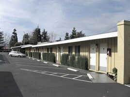 Un motel con una hilera de habitaciones, un estacionamiento y un coche aparcado al frente.