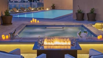 A rooftop pool area with lounge chairs, a fire feature, and potted plants.