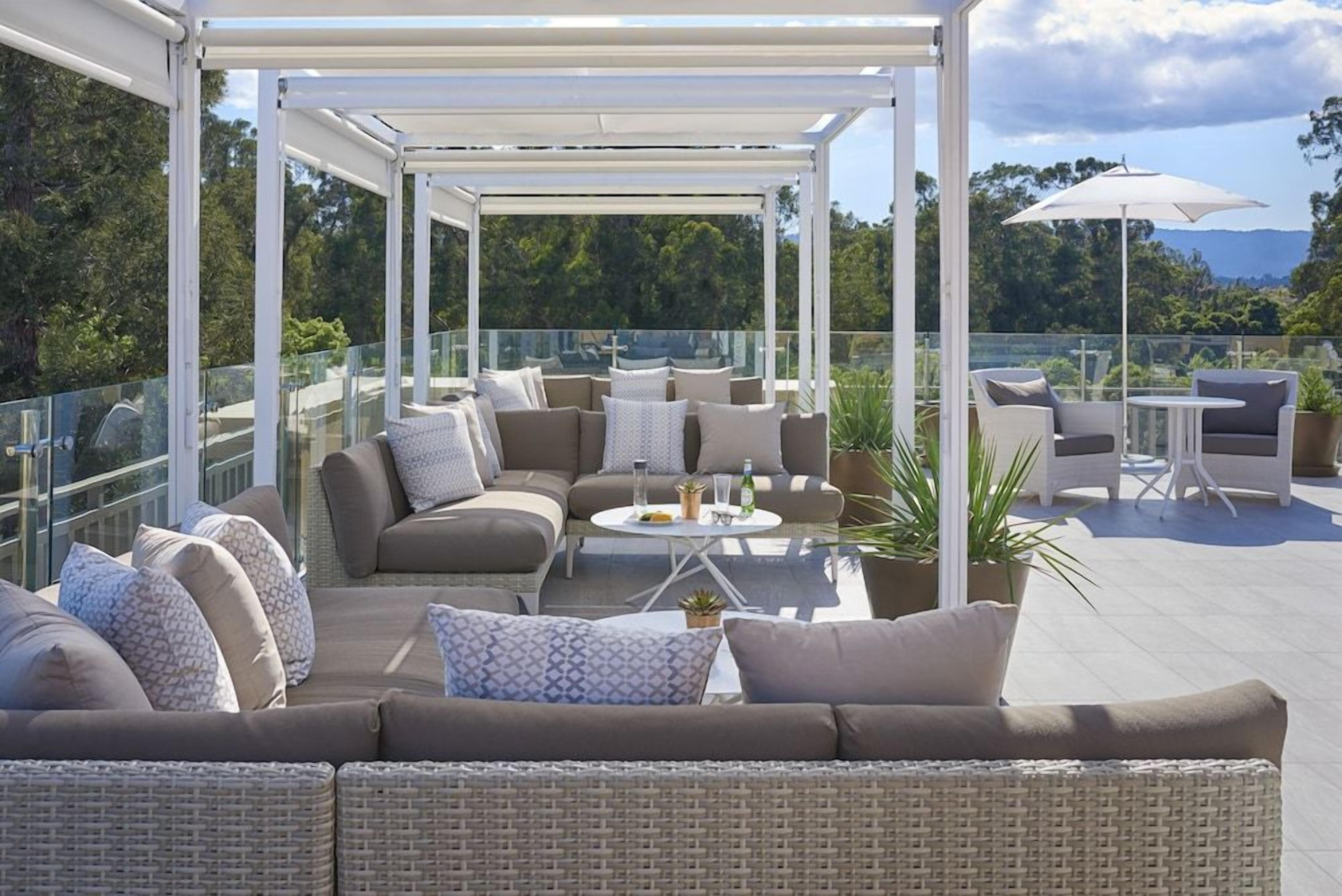 A covered outdoor seating area with a sofa, chairs, and a table, overlooking a scenic landscape.