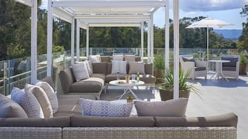A covered outdoor seating area with a sofa, chairs, and a table, overlooking a scenic landscape.
