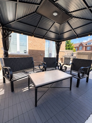Un patio exterior con zona de estar techada, una mesa y una parrilla.