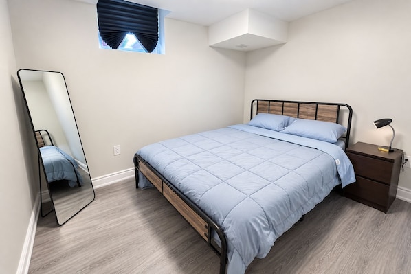 A bedroom with a bed, a nightstand, a mirror, and a window with blinds.