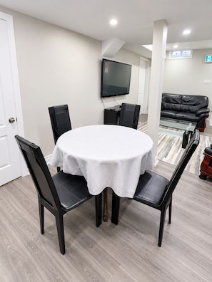 A dining area with a round table, black chairs, and a television mounted on the wall.