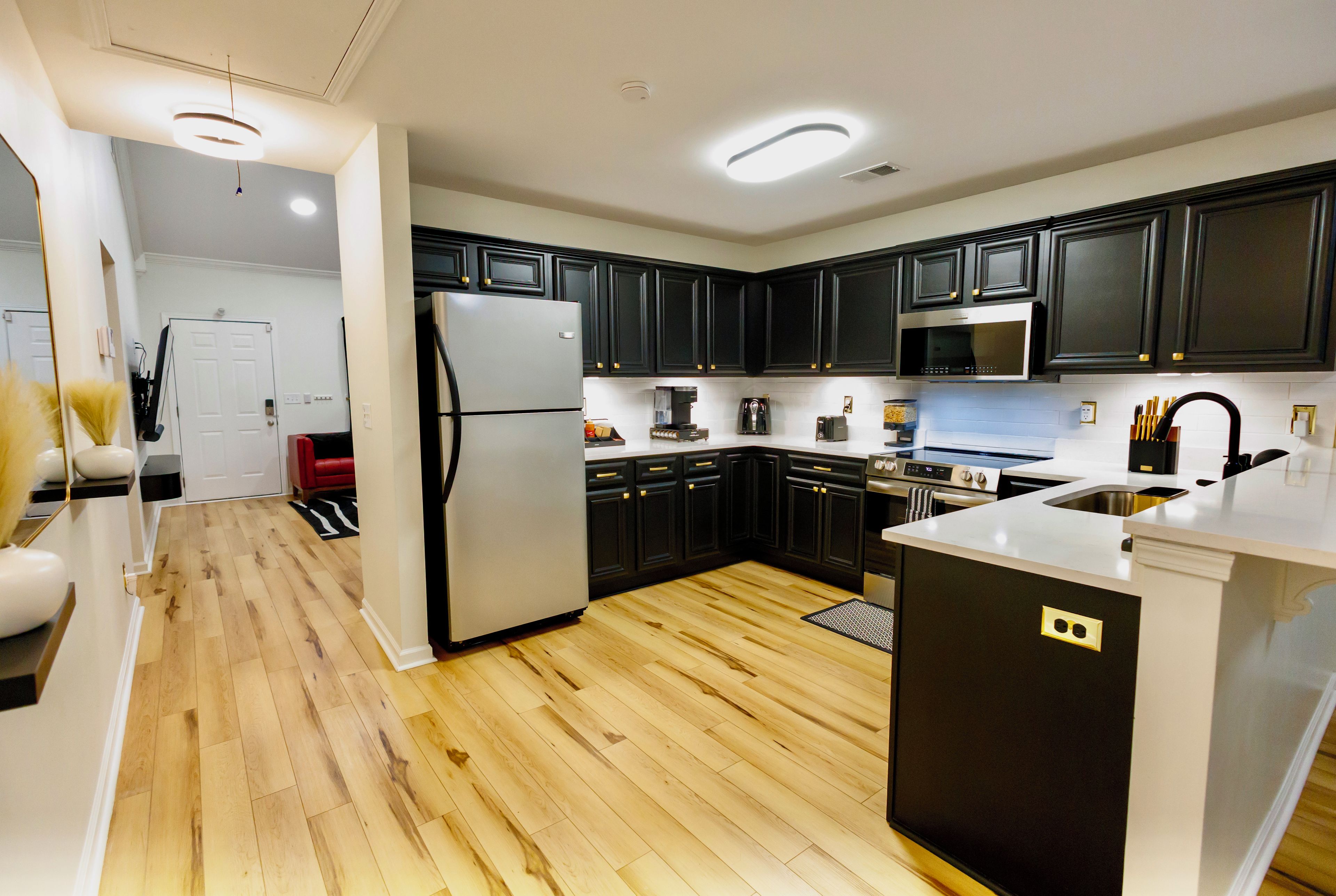 A modern kitchen with dark cabinetry, stainless steel appliances, and a wooden floor.