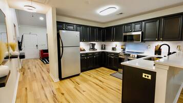 A modern kitchen with dark cabinetry, stainless steel appliances, and a wooden floor.