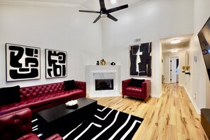 Una sala moderna con un sofá de cuero rojo, una mesa de centro negra y una chimenea. Hay obras de arte abstractas en la pared y un ventilador de techo.
