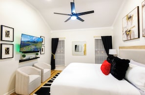 Una camera d'albergo con un letto, una televisione, un ventilatore a soffitto e opere d'arte alle pareti.