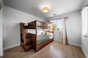 A bunk bed room with a wooden floor, a ceiling light fixture, and a window with curtains. - Saltwater pool + outdoor movies (Indio)