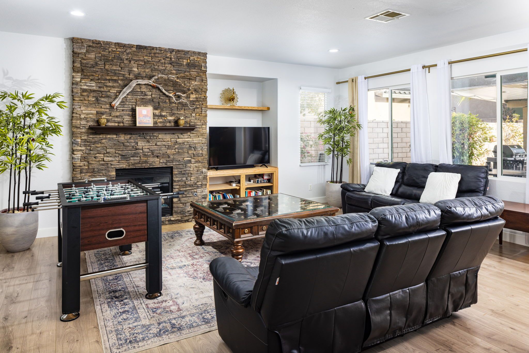 A modern living room with a stone wall, a foosball table, a leather sofa, and a flat-screen TV.