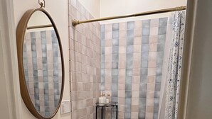 Baño con lavamanos, espejo, ducha y paredes de azulejos.