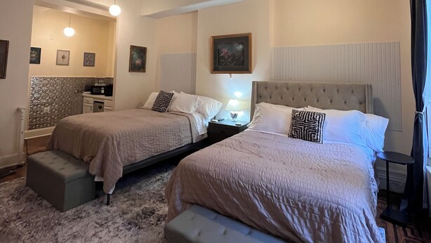 A hotel room with two beds, a sitting area, a vanity, and a ceiling fan.