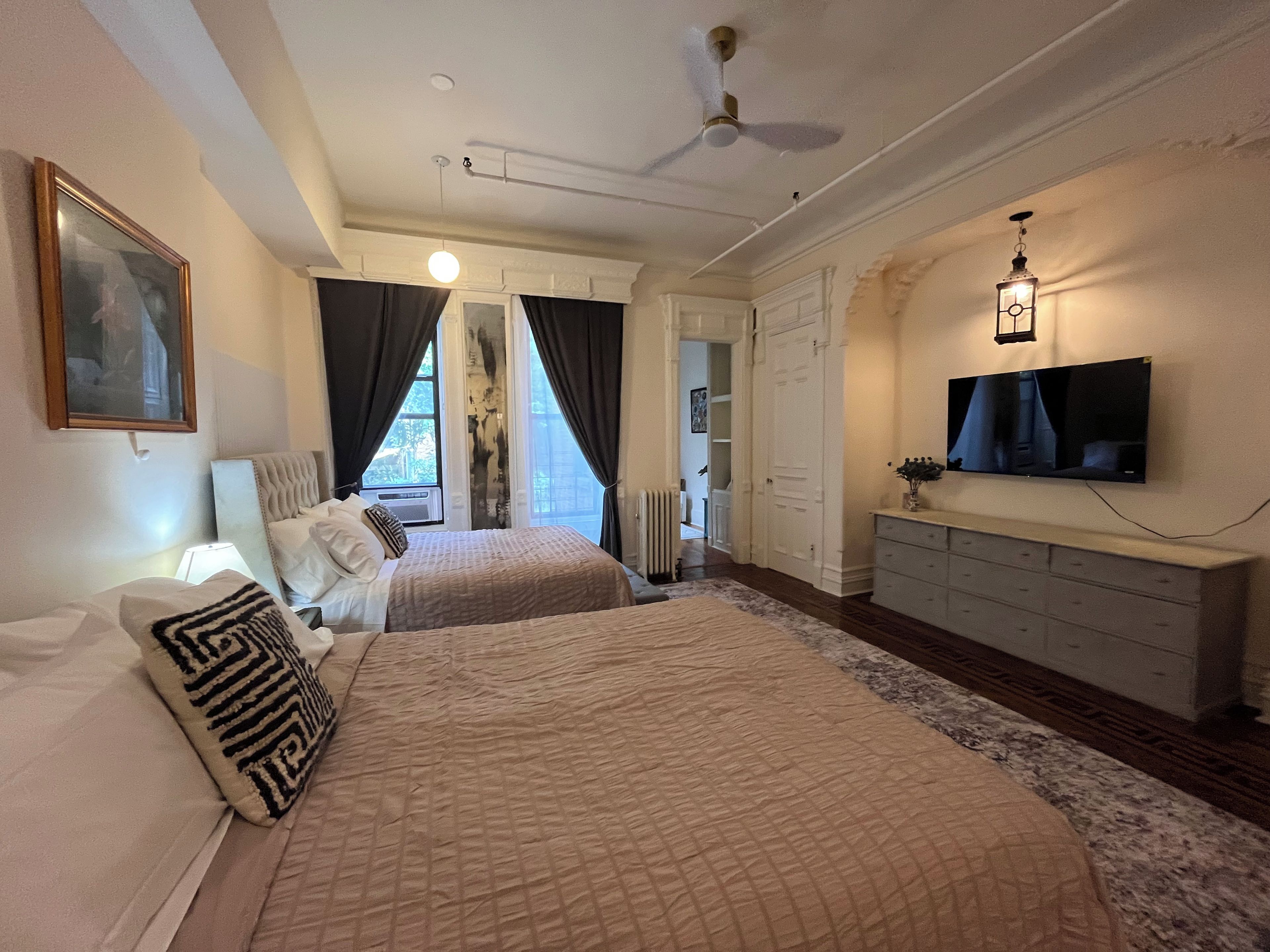 A bedroom with two beds, a ceiling fan, a TV, and a dresser.