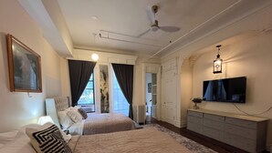 Un dormitorio con dos camas, ventilador de techo, televisor y cómoda.