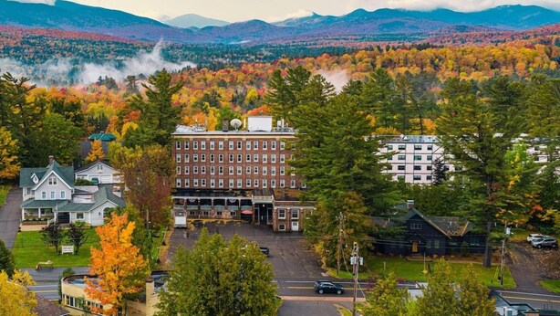 Un hotel con un edificio central rodeado de árboles de colores otoñales y montañas al fondo.