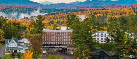A hotel with a central building surrounded by autumn-colored trees and a mountainous backdrop.