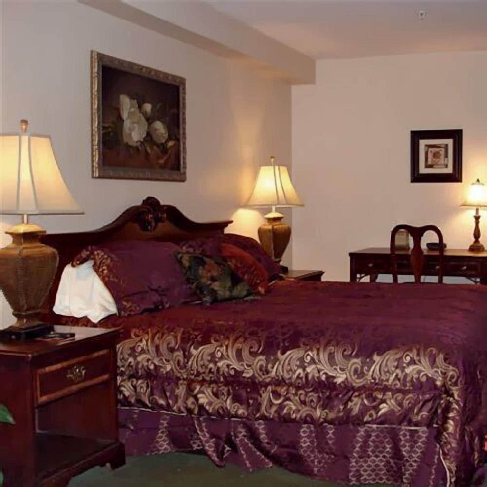A hotel room with a bed, two bedside tables with lamps, a painting on the wall, and a framed picture above the bed.