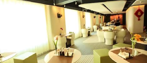 A modern hotel lobby with round tables, comfortable seating, and a large window providing natural light.