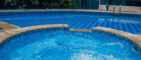 Una piscina con diseño de cuadros, un jacuzzi y una zona junto a la piscina con barandilla.