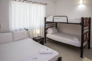 A bunk bed with a single bed beside it, a nightstand with a lamp, and a window with curtains. - 2-Bedroom Apartment Fully Furnished | Balcony with a View | Near the Beach (Cartagena de Indias)