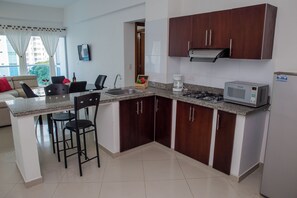 A compact kitchen with a microwave, gas stove, and a coffee maker. There is a dining area with a sofa and chairs. - 2-Bedroom Apartment Fully Furnished | Balcony with a View | Near the Beach (Cartagena de Indias)