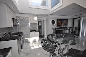 A modern kitchen with a herringbone tile backsplash, a dining area with a glass table and black chairs, and a large window providing natural light. - Sunset Views (Vancouver)