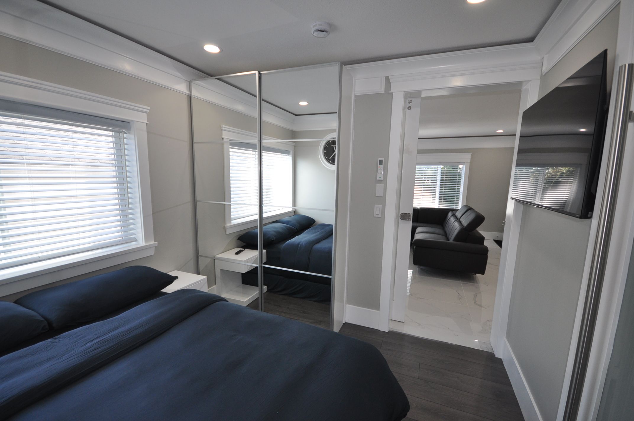 A modern bedroom with a large bed, a bedside table, a mirror, and a wardrobe.