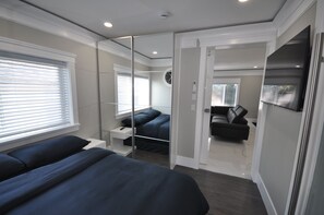A modern bedroom with a large bed, a bedside table, a mirror, and a wardrobe. - Sunset Views (Vancouver)