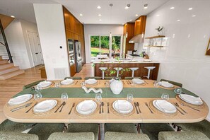 Une cuisine moderne dotée d’appareils électroménagers intégrés, un coin repas avec une longue table dressée pour six personnes, et une vue sur l’extérieur.