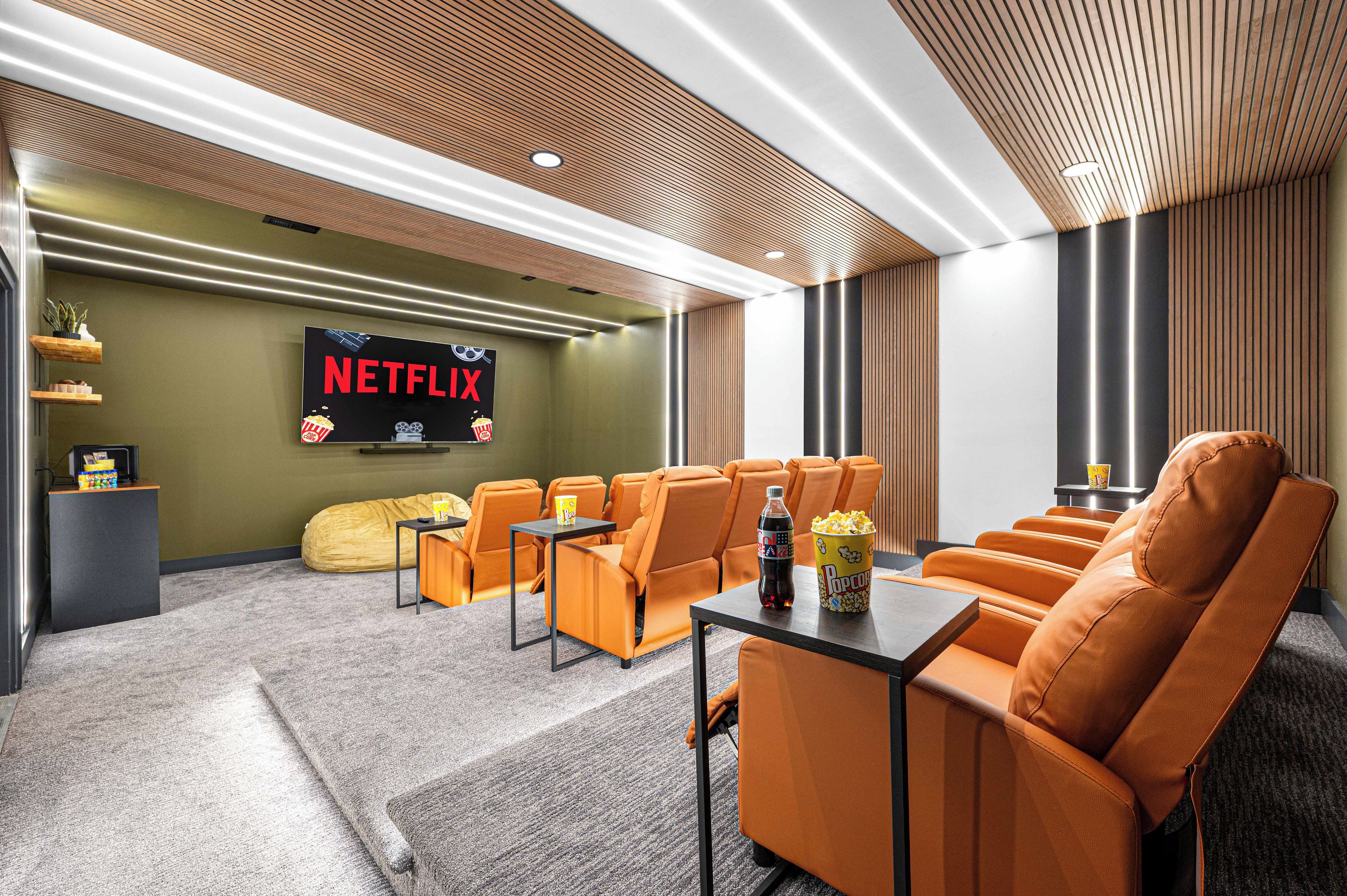A modern cinema room with orange seating, a large screen displaying 'NETFLIX', and a popcorn bucket on a table.