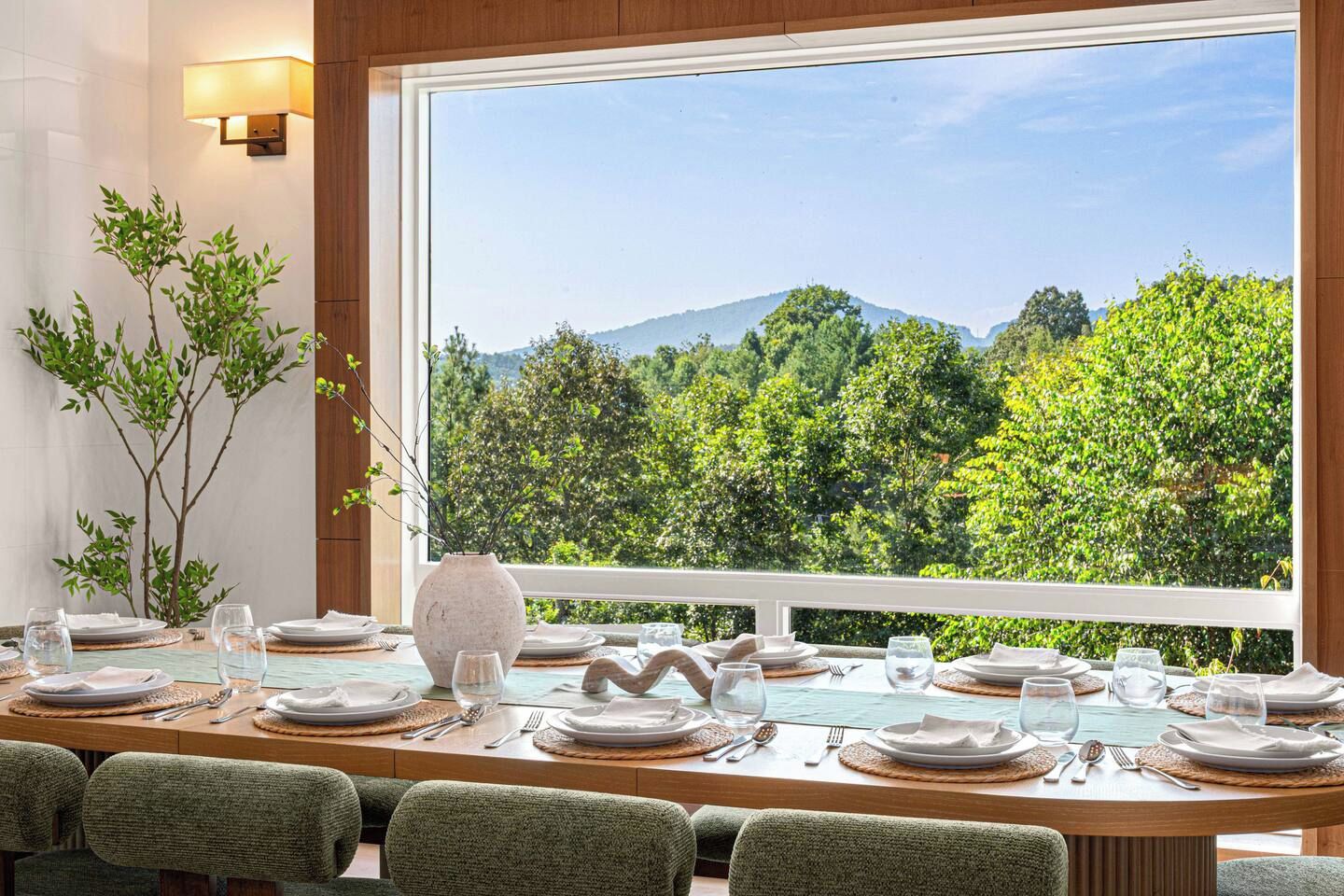 A dining area with a table set for six, a vase, and a view of a forested landscape.