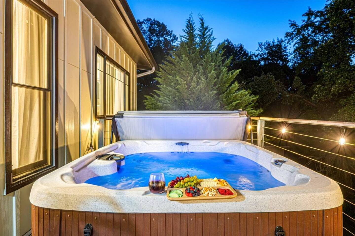Una vasca idromassaggio con un pontile in legno, circondata da un parapetto, e una casa in legno sullo sfondo.